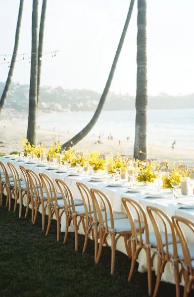 Reception tablescape showcasing outdoor reception decor, with yellow florals, near palm trees on a sandy beach by the ocean.