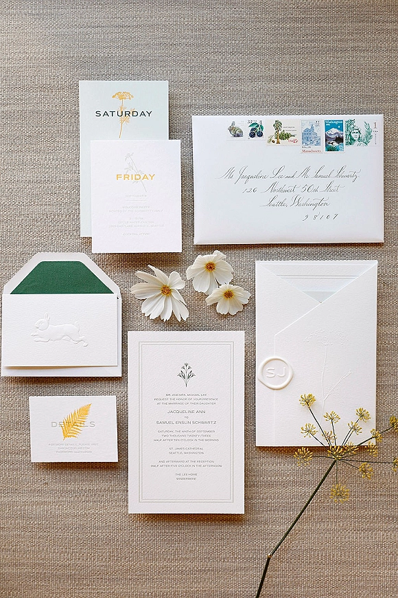 Wedding invitation suite with letterpress wedding invitations, wax-sealed envelopes, vintage stamps, and wildflowers on linen backdrop