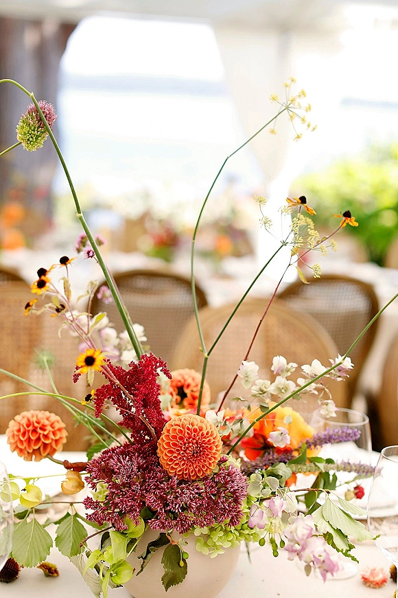 Wedding centerpiece with wildflower wedding centerpiece dahlias and greenery in bud vases beside clear wine glasses on a tented reception table