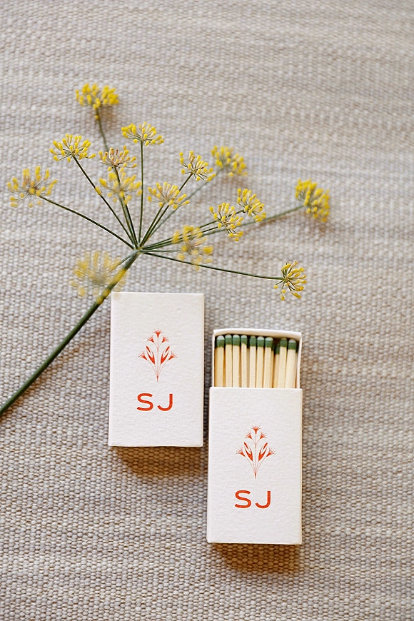 Wedding matchboxes with custom matchbox favors featuring monogram initials and yellow floral illustration on soft linen fabric flat lay