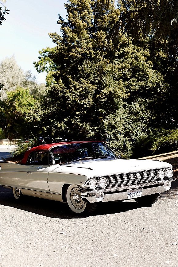 Vintage wedding car classic convertible with a red soft top, chrome grille, and whitewall tires parked on a leafy driveway in daylight