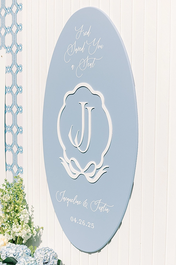 Wedding welcome sign with calligraphy lettering, monogram, and blue hydrangeas against a white paneled wall and blue tile backdrop