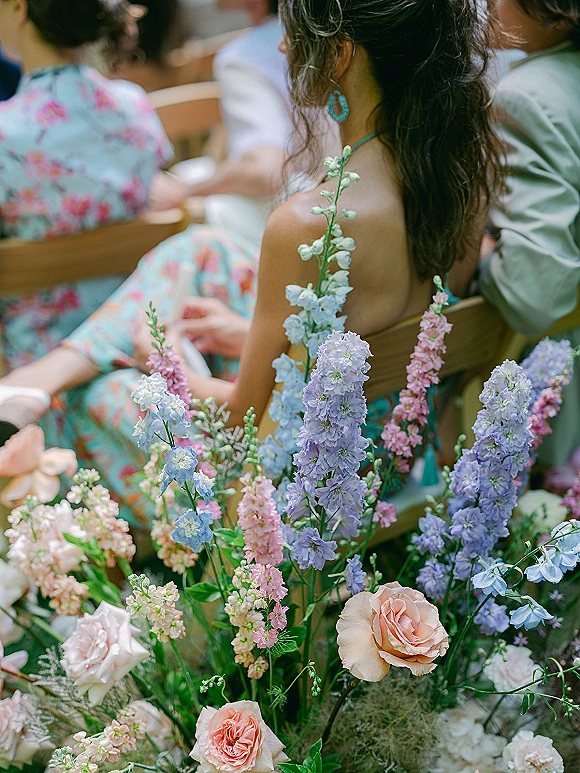 Wedding guest portrait featuring turquoise statement earrings and a teal spaghetti strap dress beside wooden ceremony chairs and pastel aisle florals