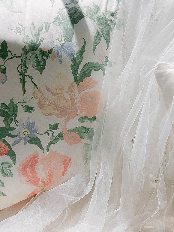 Wedding veil draped over a white chair, cathedral veil tulle cascading softly against pastel floral wallpaper backdrop