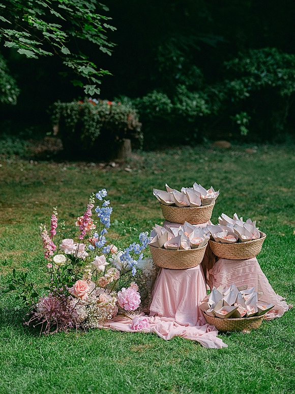 Petal toss setup with wedding petal toss baskets filled with flower petals and paper cones beside pink draped fabric on a lawn
