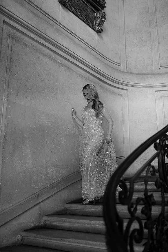 Bridal portrait in a beaded wedding dress, bride descending a curved stone staircase with wrought iron railing, holding her train