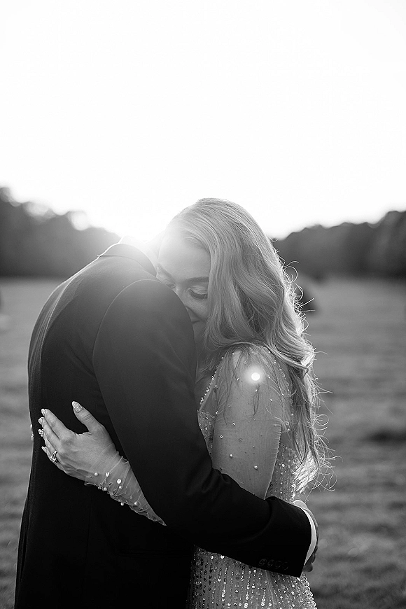 Couple portrait, black and white wedding portrait of bride and groom embracing with forehead touch, backlit in an open field at sunset