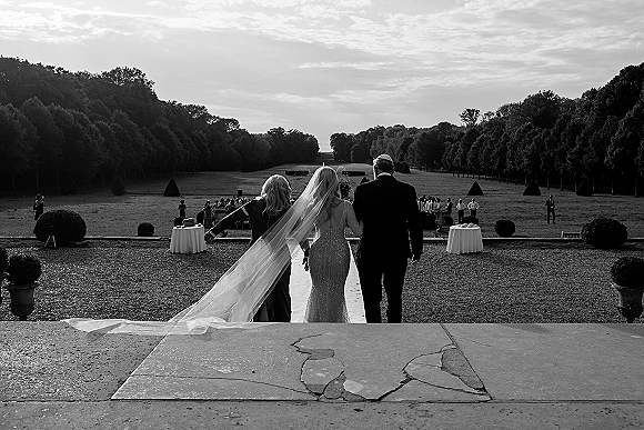 Wedding processional as bride walking down aisle in a long veil and bridal gown along an outdoor runner on a tree-lined lawn