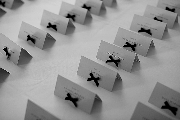 Wedding place cards with black ribbon bows and printed names, folded on a white tablecloth at a reception table for seating details