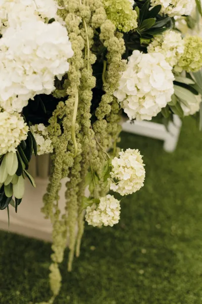 Wedding floral arrangement of white hydrangea wedding flowers with trailing hanging amaranthus and greenery on a blurred garden lawn backdrop