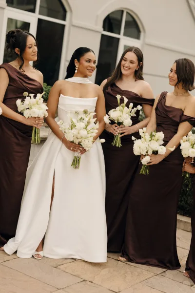 Bridal party portrait of bride with bridesmaids in brown dresses holding white calla lily bouquets on stone steps by arched windows