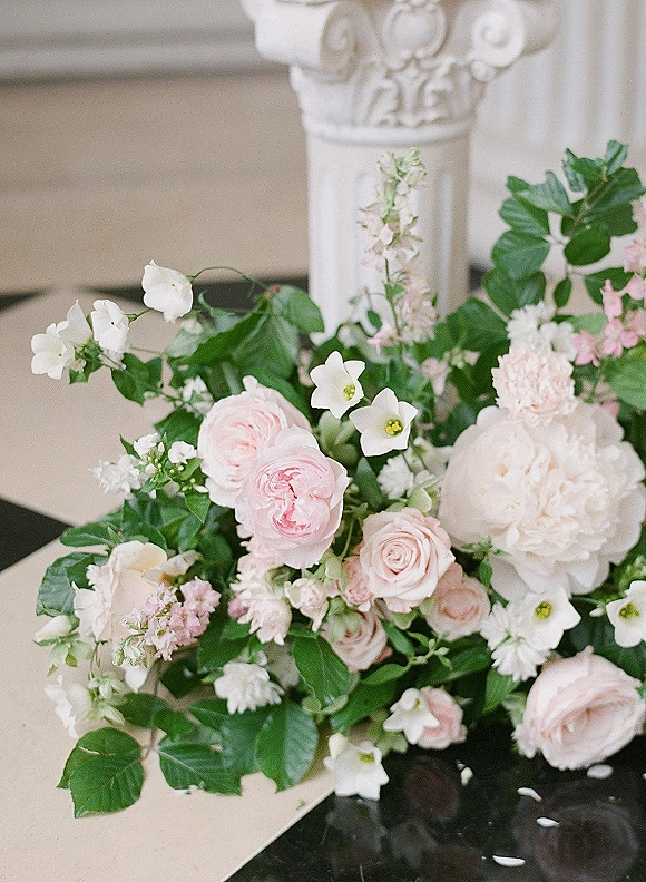 Wedding floral arrangement with blush and white centerpiece of roses, peonies, and greenery on a stone ledge by a white column