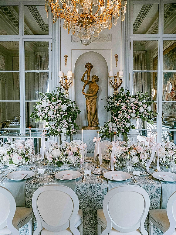 Reception tablescape with luxury wedding tablescape details, blush and white roses, greenery, taper candles, gold flatware under a chandelier