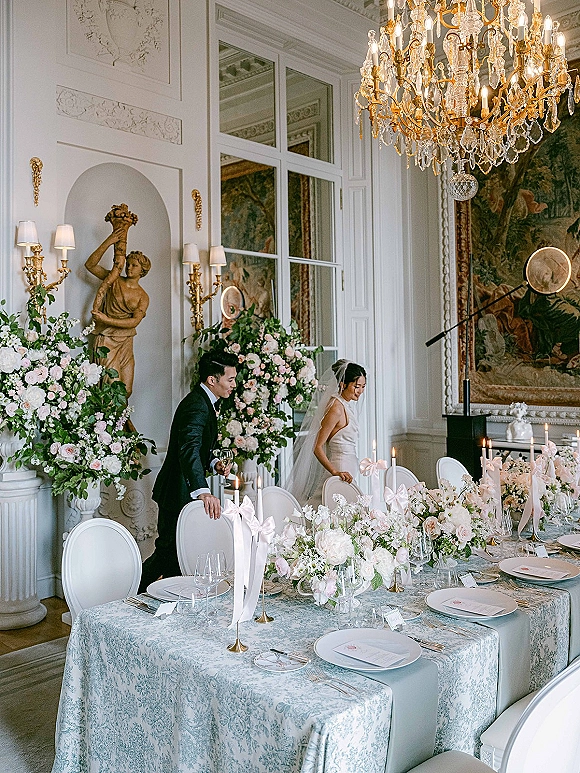 Reception tablescape with luxury wedding tablescape florals, taper candles, ribbon bows, and place settings beneath a chandelier and mirror walls