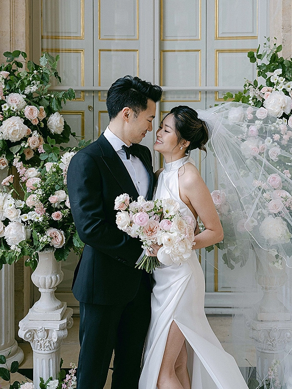 Couple portrait of bride and groom portrait with a rose bouquet, forehead touching by paneled double doors framed with floral urns