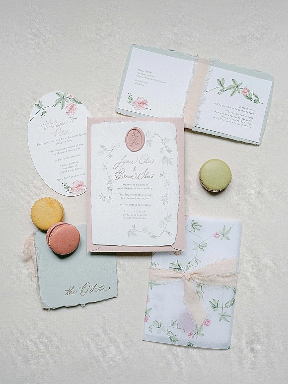 Wedding invitations arranged as a floral wedding invitation suite with a pink wax seal on deckled paper over linen fabric backdrop