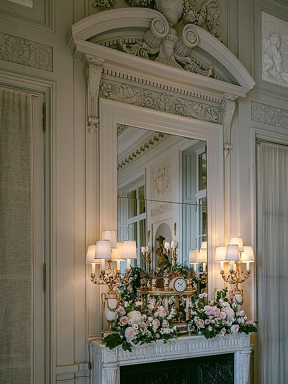 Mantel floral decor with wedding mantel flowers in blush roses and greenery, framed by an ornate mirror, candelabras, and paneled walls
