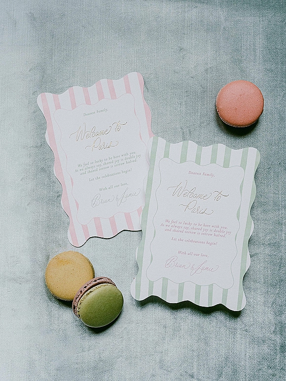 Wedding stationery suite with wedding welcome card in calligraphy, scalloped edge and striped papers, plus macarons on linen backdrop