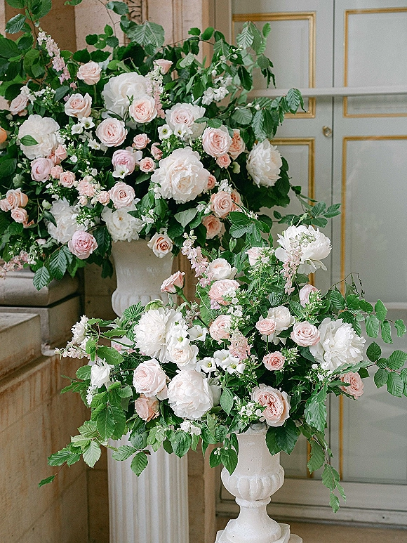 Wedding floral arrangements of blush and white wedding flowers in white urn pedestal vases with peonies, roses, and greenery by paneled doors