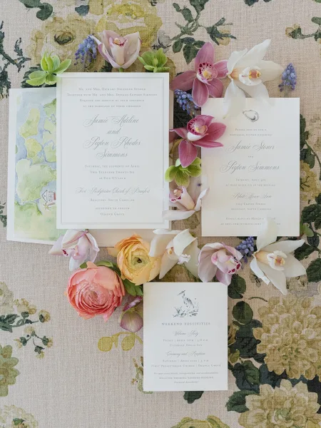 Wedding invitation suite arranged in a floral invitation flat lay, accented with orchids on a linen textile backdrop