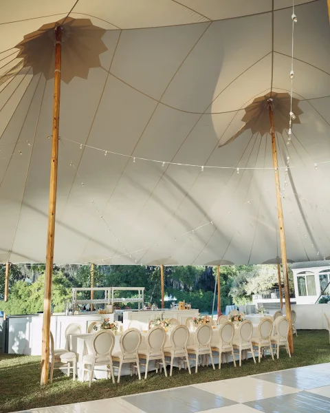 Tent reception decor for a sailcloth tent wedding featuring warm string lights beneath the canopy on a leafy garden lawn.