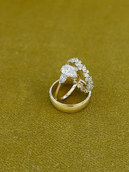Wedding rings featuring a pear shaped engagement ring paired with a diamond band, styled on green velvet fabric.