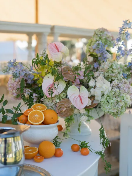 Wedding centerpiece featuring a fruit and flower arrangement with fresh oranges accenting airy blooms under a tent canopy.