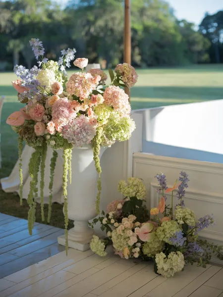 Ceremony flowers create an elegant altar flower arrangement in a classic white urn, set on a grass lawn beneath a tent.