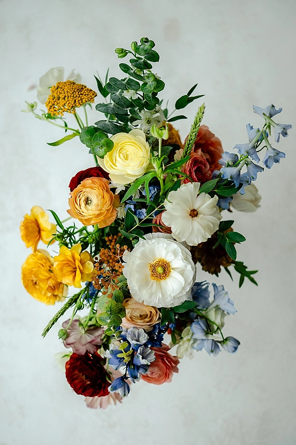 Wedding bouquet with colorful bridal bouquet blooms of ranunculus, wildflowers, and eucalyptus greenery against a clean white backdrop