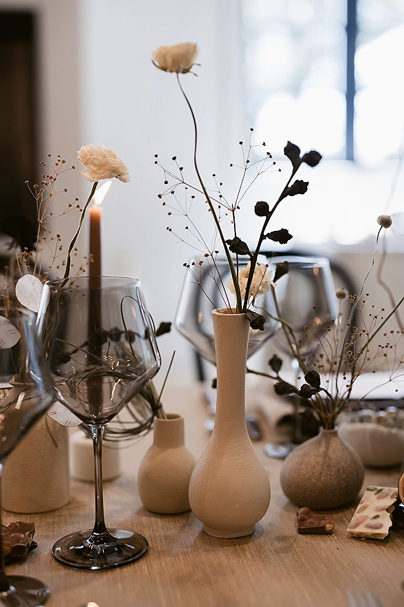 Reception tablescape with minimal wedding tablescape styling, ceramic and bud vases of dried and white flowers, taper candle, wine glasses in window light