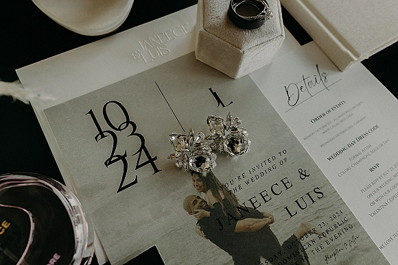 Invitation suite wedding invitation flat lay with rings in a box, crystal earrings, wax-sealed envelope, and perfume on a dark tabletop