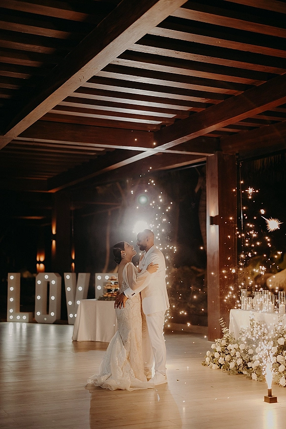 First dance with sparkler first dance fountains as bride in lace gown and groom in suit sway on an indoor dance floor under wood beams