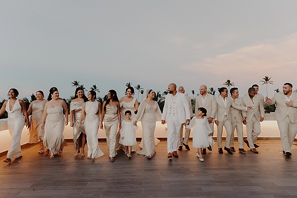 Wedding party portrait of bride and groom walking with bridesmaids and groomsmen on a rooftop terrace under palm trees in sunset light