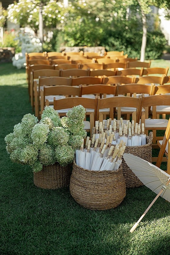 Ceremony seating with outdoor ceremony chairs in neat rows, wood folding chairs with cushions, baskets of programs and parasols on a sunny lawn