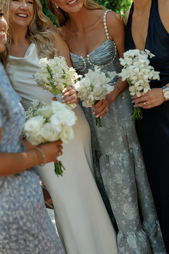 Bridesmaid portrait with bridesmaids holding bouquets of white flowers, mix-and-match satin and navy dresses, against green foliage outdoors