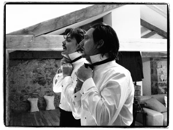 Getting ready moment as the groom ties a bow tie in a rustic loft with exposed beams, a stone wall, and warm wood floors