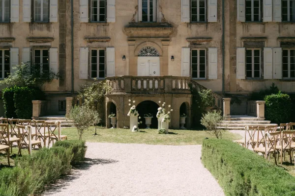 Outdoor ceremony setup styled with garden ceremony decor and crossback chairs facing a stone staircase and historic facade on a gravel aisle.