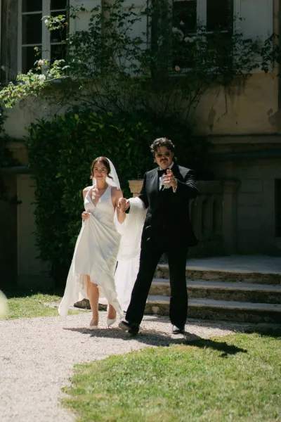 Couple portrait of a bride and groom walking hand in hand down stone steps beside an ivy wall, her long veil trailing in natural garden light.