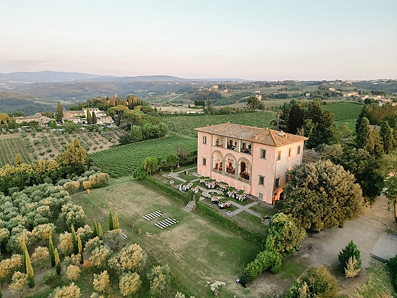 Wedding venue aerial view of a villa courtyard with outdoor reception tables and string lights, surrounded by vineyards and rolling hills