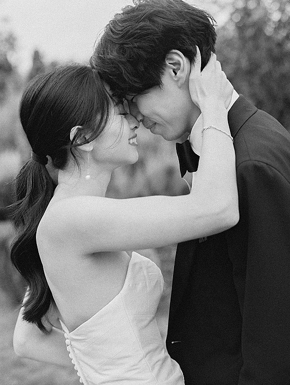 Wedding couple portrait with a wedding forehead touch as the bride cradles the groom’s face, nose to nose in soft light with trees behind