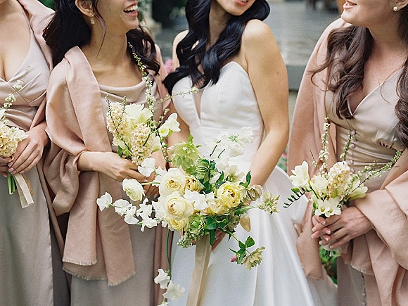 Bridesmaid portrait with bride and bridesmaids in neutral dresses holding ivory rose bouquets with greenery on outdoor stone steps
