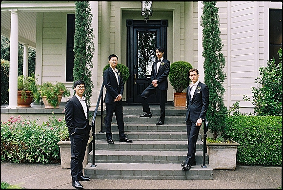 Groomsmen portrait of a wedding party in black tuxedos with bow ties and boutonnieres posing on front porch steps by a black door