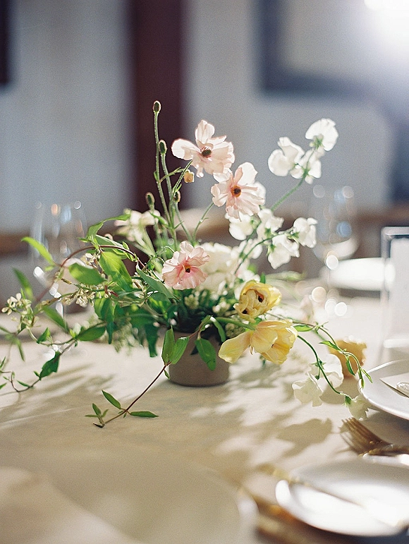 Reception centerpiece with a wildflower wedding centerpiece in bud vases and greenery on a white tablecloth with plates and wine glasses