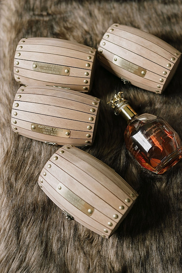 Groomsmen gifts in engraved groomsmen gifts boxes with metal rivets and a liquor bottle arranged as a flat lay on fur surface