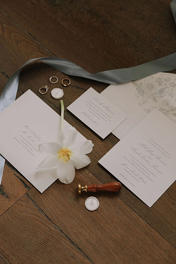 Invitation suite wedding invitation flat lay with RSVP card, envelopes, wax seals, silk ribbon, rings and a white flower on wooden floor