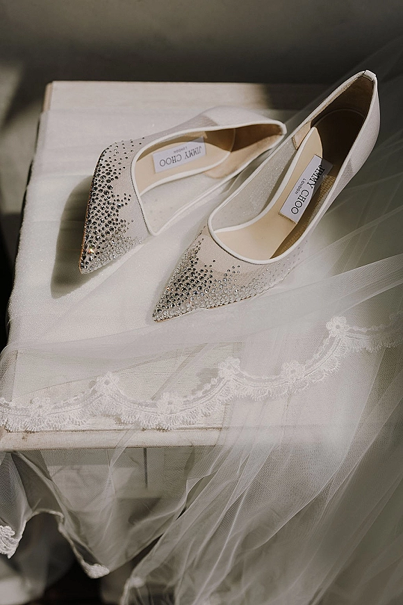 Bridal shoes in a wedding shoe flatlay, sparkly rhinestone pointed-toe heels on a box with lace veil and tulle nearby