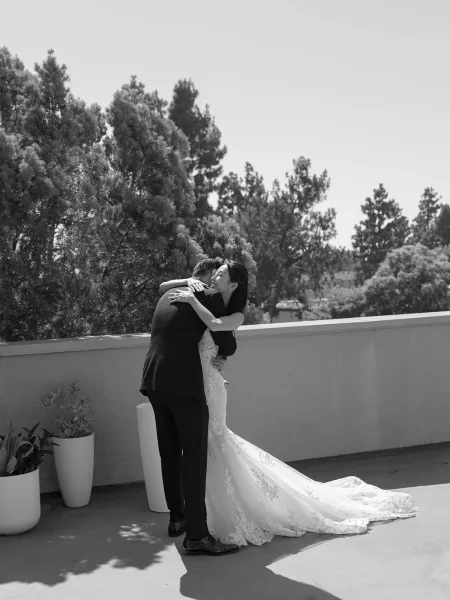Wedding couple portrait of bride and groom embracing, her strapless lace dress with long train flowing on an outdoor terrace by potted plants