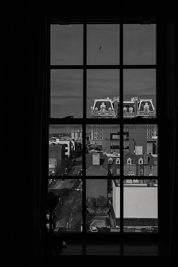 City window view through a large grid window, framing historic rooftops and skyline above a street under a cloudy sky