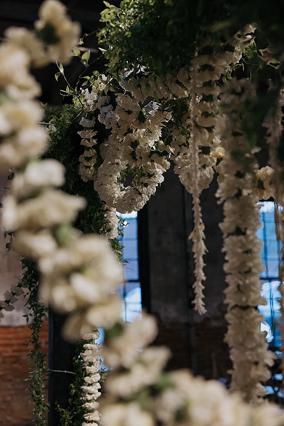 Hanging floral installation with hanging wedding flowers, white blooms and greenery cascading over a floral arch in a dark-walled venue