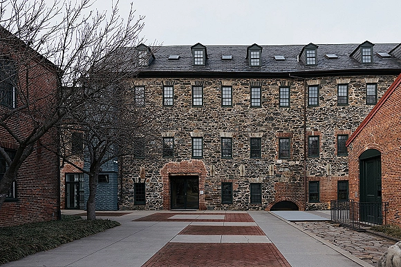 Stone courtyard venue with historic stone building exterior, brick buildings and black-framed windows along a cobblestone path under overcast skies